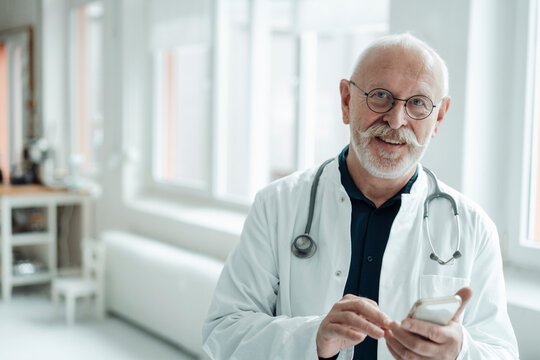 Smiling senior doctor holding mobile phone at hospital