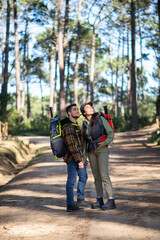 Portrait of loving couple of young hikers. Caucasian man with beard and woman in cap with big backpacks holding hands and looking up. Hobby, nature, love concept