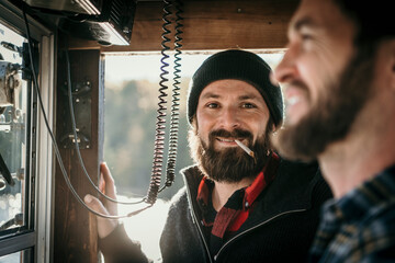 Man smoking cigarette standing with friend in control room of boat