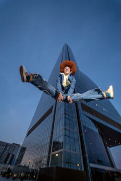 Smiling woman in redhead Afro hairstyle jumping in front of Skyscraper
