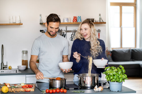Happy woman serving spaghetti standing by boyfriend in kitchen