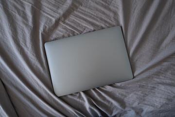 Working at home concept. Laptop in bed. Flat lay, top view minimalistic workspace background. Relaxing working process.
