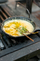 mantequilla derretida con romero  en sarten de hierro  sobre la parrilla. 

mantequilla derretida condimentada en el asador.