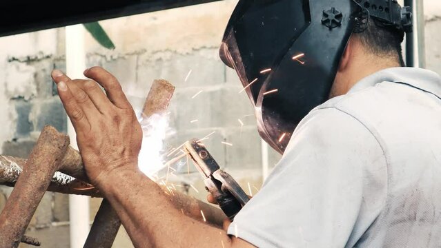 Professional welder employing industrial welding machine to put together two pieces of metal creating a metalic structure as part of his daily work at a local small business