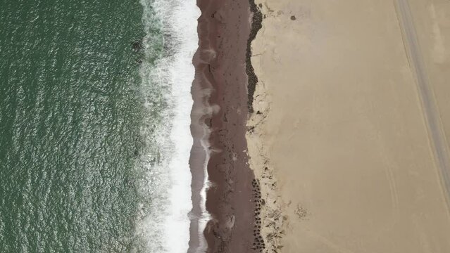 Vertical aerial pattern: Green ocean waves onto desert cliff sand