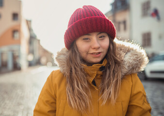 Happy young woman with Down syndrome weraing parka and hat, walking in town and looking at camera.