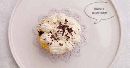 Top view of a cupcake with cream and chocolate chips on a plate with a wish for a good day. Wide view