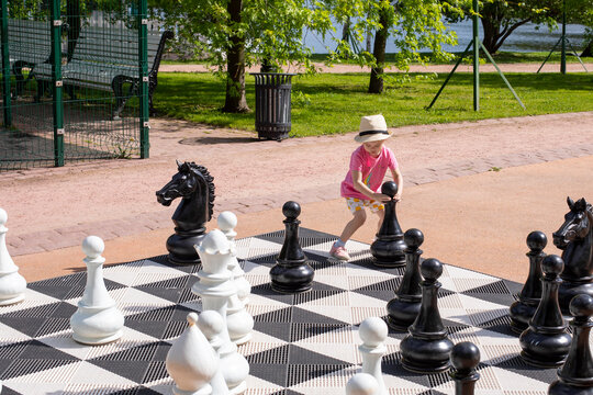 Little caucasian girl wearing a straw hat plays giant chess outdoors