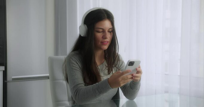 Close up of the attractive young girl in the big headphones turning on the music on her smartphone and moving