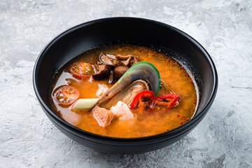 Traditional spicy Thai soup Tom Yum with shrimp and seafood in ceramic bowl on stone background