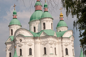 Fototapeta na wymiar Christian orthodox white church with green domes with gold crosses. Calm blue sky above