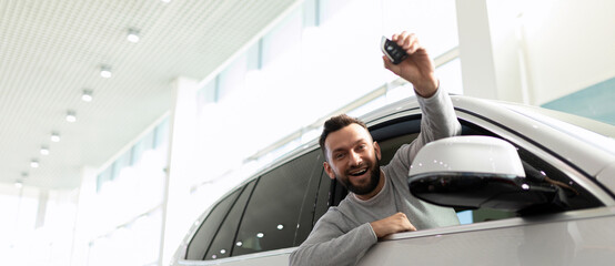 happy owner of a new car demonstrate car keys in a car dealership