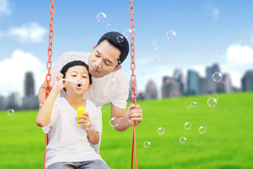 Child blowing soap bubbles with father at park
