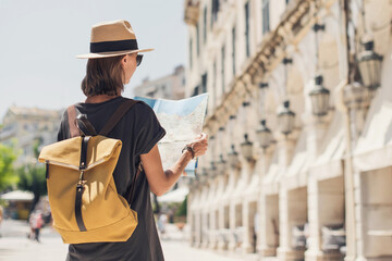 Travel concept, beautiful tourist woman standing with map in Kerkyra old town during vacation, cheerful student girl traveling abroad in summer, Corfu island, Greece
