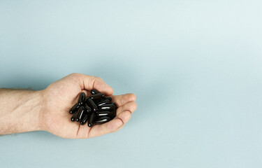 Men's hand with capsules of black color, vitamins for men on a blue background. The concept of a healthy lifestyle, with space for text.