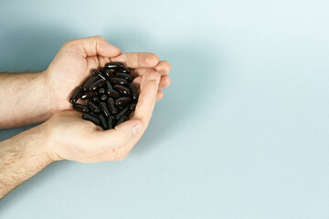 Men's hands, filled with capsules of black color, vitamins for men on a blue background. The concept of health with space for text.