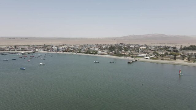 Aerial pan right along desert port town, Paracas' waterfront in Peru