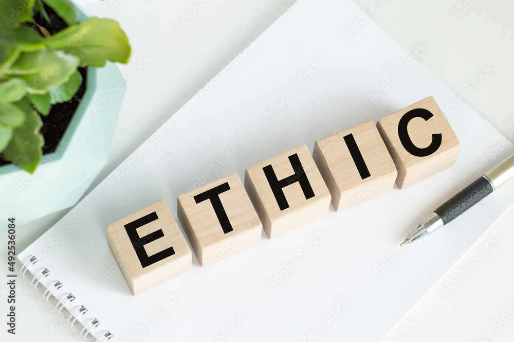 Poster ethic word written on wooden blocks on a table on a notepad background next to a pen and a potted fl