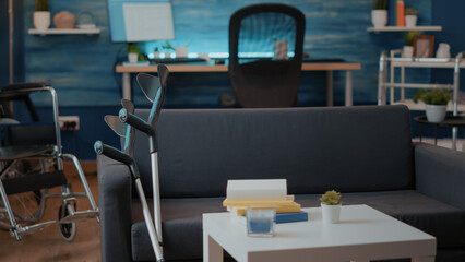 Medical crutches on couch used by person with physical disability. Empty living room with walking support sticks and wheelchair to give aid and accessibility for transportation.