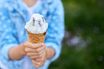 Unrecognizable girl with italian ice cream cone in hand,  resting in park on summer day, child enjoying ice cream outdoor, happy holidays, summertime