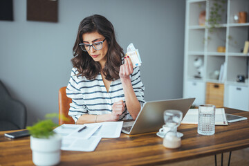 A business woman who pays her bills online at home using a laptop computer. He calculates how much...
