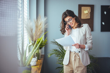 A young business woman standing in a hotel room using a mobile phone. A woman stands in a hotel...
