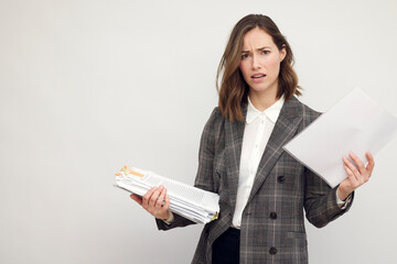 Frustrated and confused female worker and business woman holding a pile of paperwork. Looking...