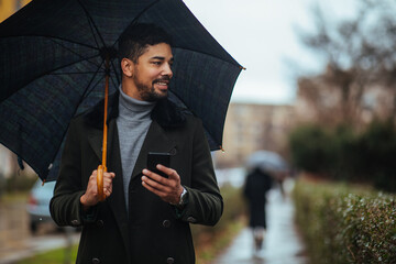 Businessman texting under umbrella in the rain