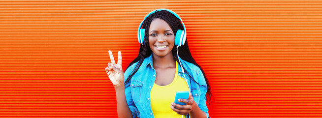 Portrait of happy smiling young african woman in headphones listening to music with smartphone