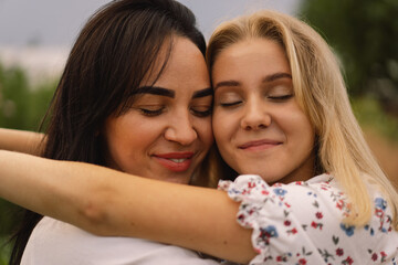 Obraz premium Happy mother's day. A young mother with a teenage daughter spends time in the garden. Mom and her daughter teenage girl are playing, smiling and hugging. Loving single mother hugs cute daughter.