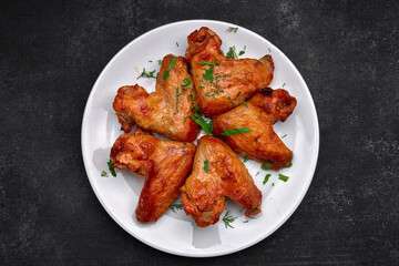 Grilled chicken wings on a plate, on a dark background