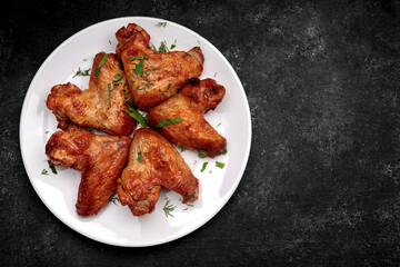 Grilled chicken wings on a plate, on a dark background