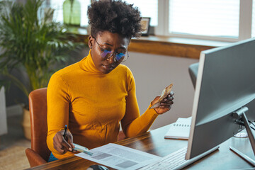 Serious young African woman wearing glasses and calculating finances, household expenses, confident...