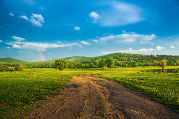 Fototapeta na wymiar Rainbow over fields and trees on a farm on the edge of Lake