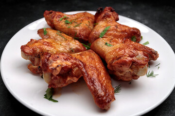 Grilled chicken wings on a plate, on a dark background