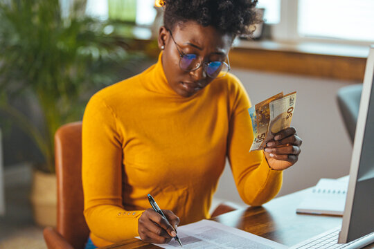 Tired young African American woman feeling stressed because of financial problems, working through finances in room all day, doesn't have enough money to pay bills