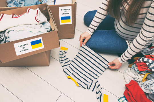 the pregnant woman is sorting baby clothes with desire to donate its for Ukrainian refugees
