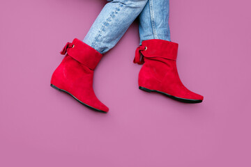 Woman's legs in blue jeans and red suede leather short angle boots without heels on blueberry color background. Copy space, top front view, flat lay.