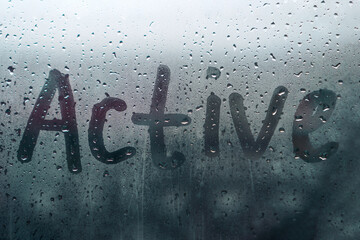 Word ACTIVE is written on the wet, fogged glass from the rain