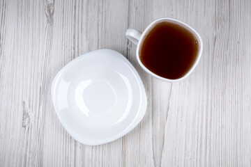Black tea in a white cup and a white plate on a wooden table, close-up. healthy drink