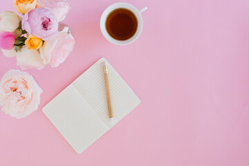 Aerial view of pink background with notebook, cup and flowers