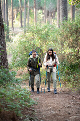 Energetic young hikers walking in forest. Caucasian man and woman in casual clothes with big backpacks trekking, going up, smiling. Hobby, nature, love concept