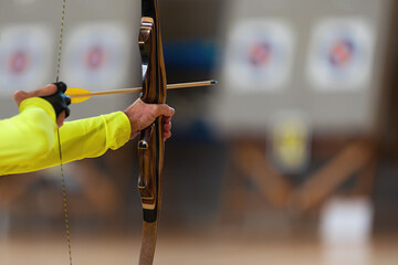 Archer holds his bow aiming at a target, archery as a sport discipline in the hall. Competition for the best shot an arrow into targets - obrazy, fototapety, plakaty