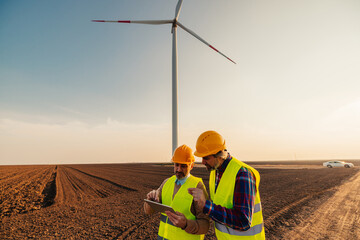 Two middle engineers using technology at windmill