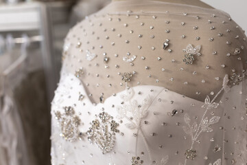 Fototapeta na wymiar Close-up of the wedding white dress on the mannequin. Rhinestones and beads, embroidery decor. Bokeh shiny elements of clothing. Copyspace, banner size