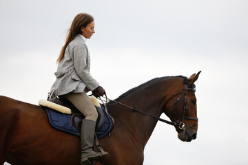 Obraz premium Beautiful young woman riding a horse on the field. Sideways to the camera. Freedom, joy, movement