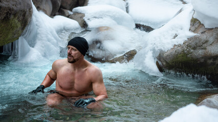 middle aged man with swimsuit, fur hat and a neoprene gloves is hardening the body  in cold river wather in the winter. Good immunity is protection against many diseases. 