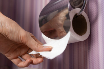 Close-up of a woman's hand pulling toilet paper in the toilet on a lilac background.