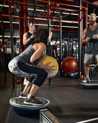 The guys tries to keep his balance on the balancing platform with fitness ball. Group exercise with the help of a fitness trainer.