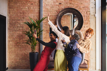 Portrait of multiethnic businesswomen taking selfie on smartphone in modern office, laughing and smiling